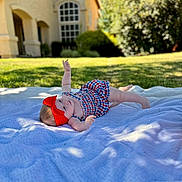 Emily joined the competition — help win amazing prizes! baby, infant, blanket, red_headband, checkered_outfit, outdoor, grass, house, sunlight, portrait, child, cute, lying_down, stretching, summer, daylight, nature, headwear, happy, skin