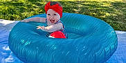 Emily is registered to the contest to win money with this photo: baby, child, inflatable_ring, red_bow, smiling, outdoor, grass, blanket, sunlight, headband, happy, summer, playtime, candid, infant, blue, greenery, portrait, cute, fun