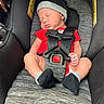 baby, newborn, car_seat, sleeping, hat, red_clothing, black_socks, infant, child, safety_harness, seatbelt, toddler, portrait, cute, indoors, resting, small_person, one_person, infant_clothing, peaceful