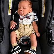 Charles is registered to the contest to win money with this photo: baby, infant, car_seat, sleeping, bow_tie, suspenders, white_shirt, shorts, sneakers, footwear, black, child, cute, resting, indoors, clothing, fashion, portrait, seatbelt, adorable