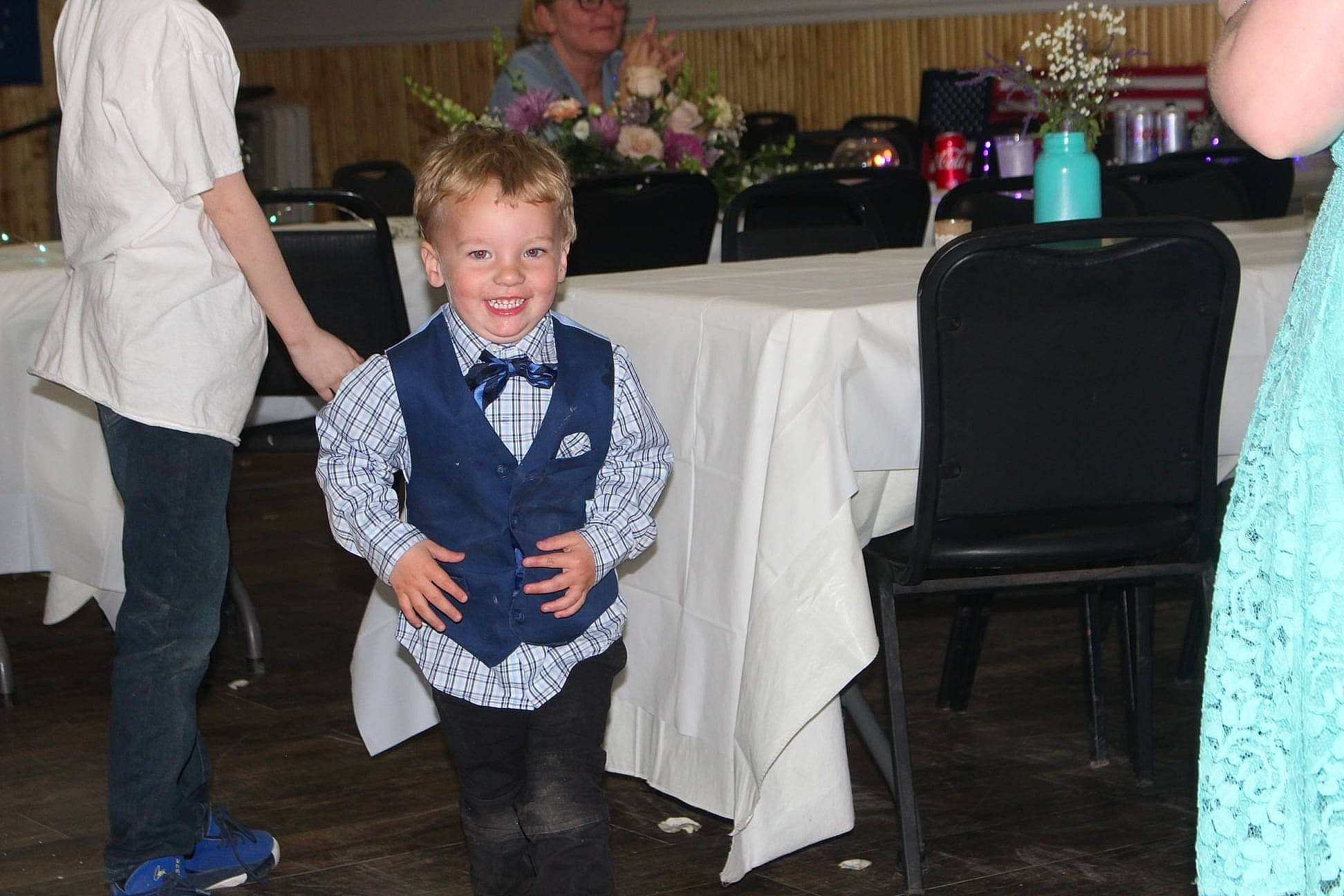 Mason is registered to the contest to win money with this photo: black, ceremony, chair, child, event, formal_wear, fun, furniture, headwear, holiday, joy, party, person, room, smile, social_group, table, tablecloth, tie, toddler