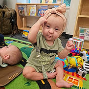 Charlotte Mae joined the competition — help win amazing prizes! baby, headband, toy, playmat, floor, child, indoor, book, colorful, playroom, infant, sitting, cute, clothing, carpet, furniture, person, young_child, smiling, playtime