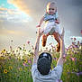 Wrenzie is registered to the contest to win money with this photo: baby, adult, flower_field, wildflowers, sky, clouds, sunlight, playing, outdoor, nature, greenery, person, hat, tattoos, child, holding, happy, summer, casual_clothing, fun