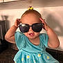 toddler, child, sunglasses, blue_dress, daisy_pattern, kitchen_counter, smile, cheeky, yellow_bow, baby, cute, indoor, person, happy, playful, portrait, young_child, fashion, accessory, casual