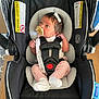 baby, infant, car_seat, pacifier, headband, pink_pants, white_socks, black_car_seat, gray_cushion, wooden_floor, warning_label, baby_gear, child, cute, small_hands, newborn, indoor, seatbelt, safety, looking_away