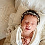 newborn, baby, sleeping, wrapped, blanket, headband, flower_crown, soft_texture, cozy, portrait, infant, cute, peaceful, hands, closeup, indoors, warm_colors, skin, head, resting