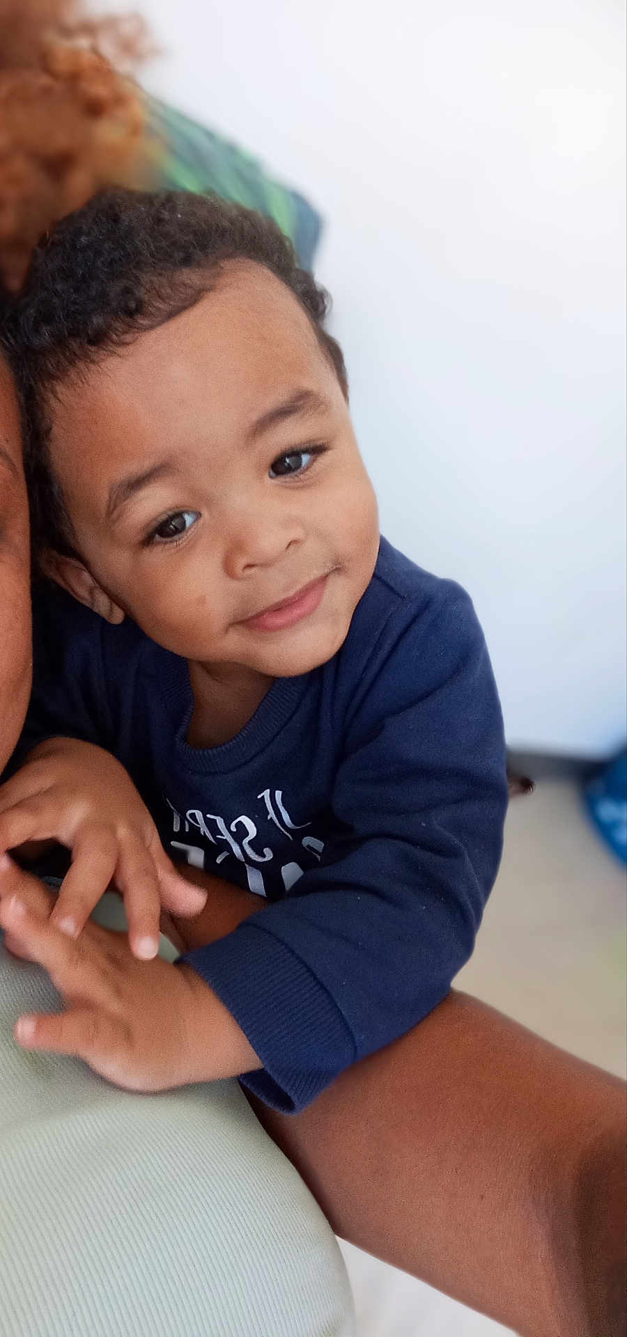 Owen participe au concours pour gagner de l'argent avec cette photo : child, toddler, smile, face, arm, clothing, blue_sweatshirt, curly_hair, indoor, person, closeup, affection, skin, hand, portrait, baby, cute, happy, young_child, warmth