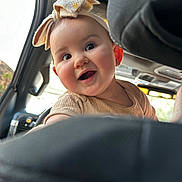 Everly is registered to the contest to win money with this photo: baby, child, smile, headband, car_interior, seat, window, light, happy, cute, infant, face, clothing, earrings, portrait, young, people, vehicle, travel, joy
