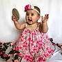 Everly is registered to the contest to win money with this photo: baby, child, girl, floral_dress, flower_headband, pink_flowers, milestone, nine_months, plaque, white_background, smiling, happy, cute, portrait, sitting, decorative_flowers, celebration, hands_up, infant, studio_photo