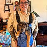 Donut joined the competition — help win amazing prizes! person, puppy, dog, pet, animal, portrait, smiling, glasses, indoor, home, backpack, carrier, overalls, shirt, tattoos, jewelry, couch, shelves, flag, toys