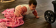 Kaylani is registered to the contest to win money with this photo: baby, crawling, blanket, wood_floor, indoor, furniture, baby_gear, chair, baby_bouncer, pink, cozy, child, person, flooring, home, infant, clothing, toy, living_room, wheel