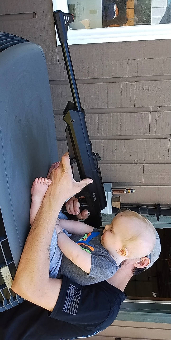 John is registered to the contest to win money with this photo: air_gun, arm, baby, baby_toddler_clothing, child, comfort, elbow, engineering, finger, gesture, gun_barrel, human_leg, joint, knee, machine, muscle, person, shooting, thigh, thumb