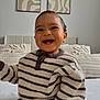 baby, smiling, striped_sweater, child, indoor, bed, pillows, abstract_art, happy, cute, portrait, person, young_child, cozy, knitwear, infant, room, home, sitting, face