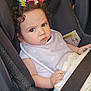 toddler, child, car_seat, curly_hair, blanket, plush_toy, seatbelt, baby_bib, indoor, person, cute, expression, car_interior, child_safety, soft_toy, infant, baby, seat, serious_expression, clothing