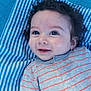 baby, child, curly_hair, smile, blue_eyes, striped_shirt, gray_shirt, blanket, striped_blanket, lying_down, infant, cute, happy, portrait, closeup, face, skin, young_child, indoors, person