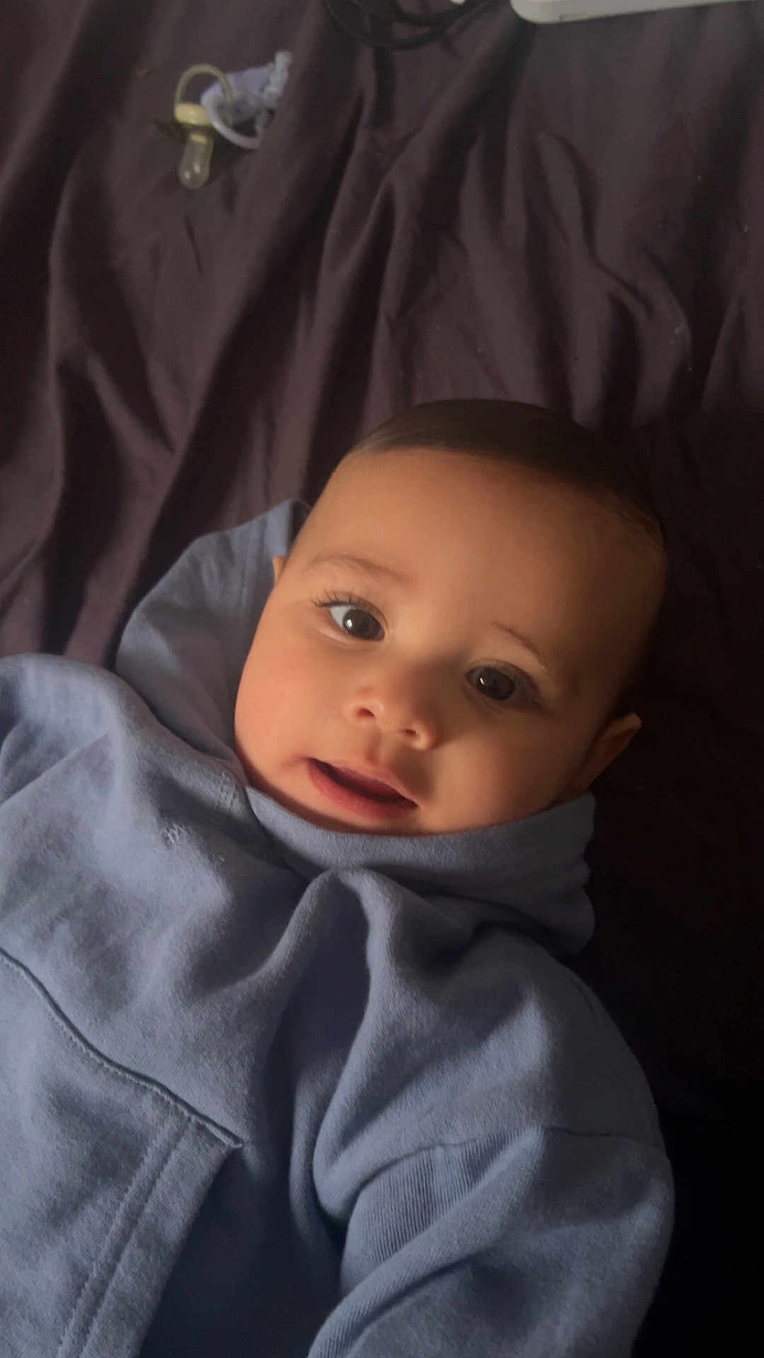 Kaïs a rejoint le concours — aidez-le/la à gagner de superbes lots ! baby, child, face, hoodie, blue_clothing, indoor, pacifier, portrait, cute, infant, smile, young_child, lying_down, warm_clothing, cozy, person, soft_light, dark_background, closeup, head