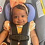 baby, child, car_seat, seatbelt, bow, headband, smile, cute, infant, clothing, sitting, child_safety, portrait, happy, young, person, closeup, indoor, car, seat