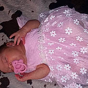 Anora is registered to the contest to win money with this photo: baby, sleeping, pacifier, pink_dress, floral_pattern, blanket, infant, cute, peaceful, child, rest, soft_texture, newborn, toddler, hand, face, lying_down, adorable, young, indoors