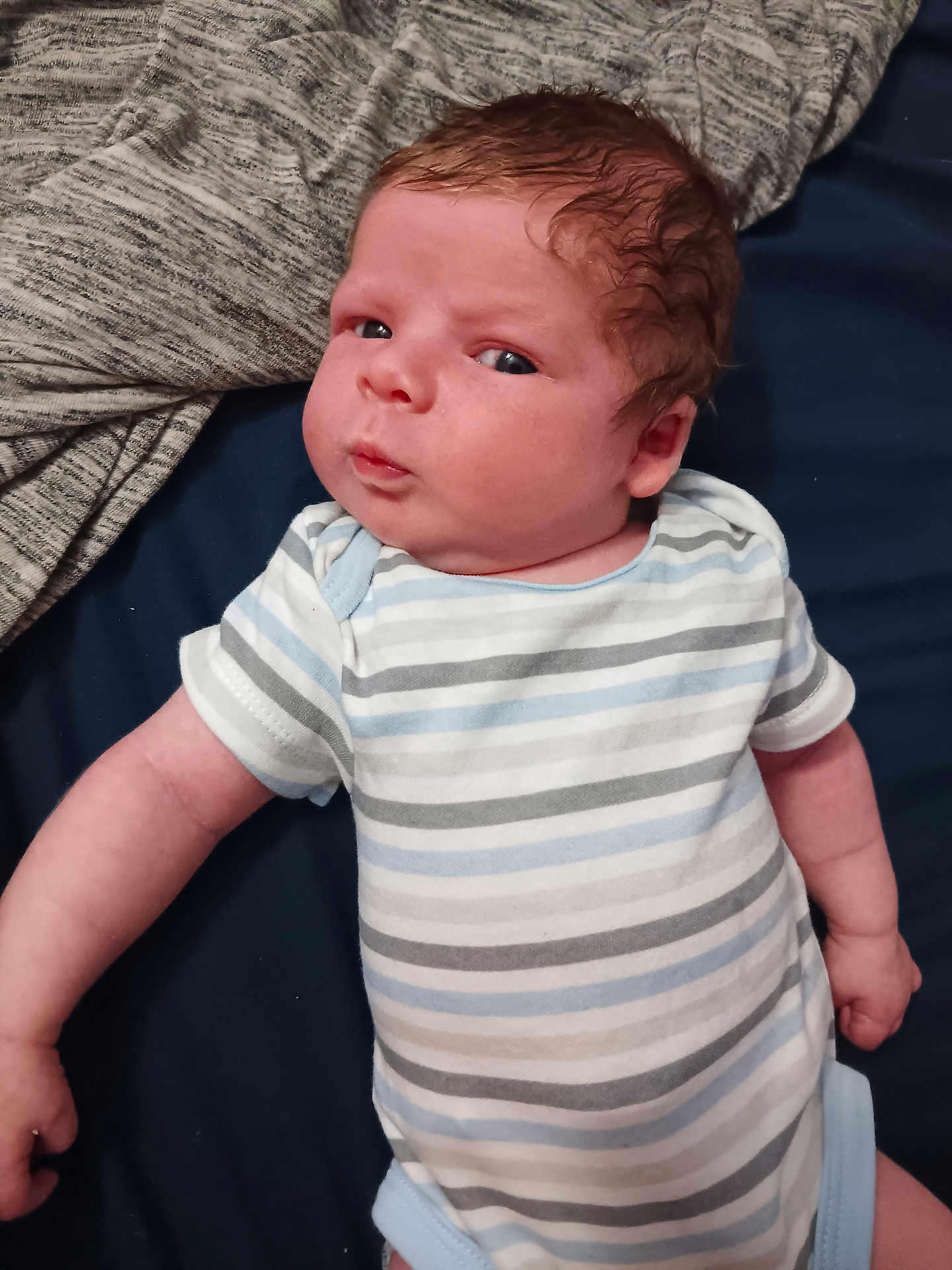 Ryker joined the competition — help win amazing prizes! baby, infant, striped_onesie, clothing, lying_down, curious_expression, face, skin, arm, blanket, fabric, textile, comfort, newborn, child, person, indoor, resting, cute, portrait
