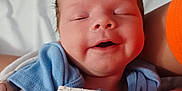 Ryker is registered to the contest to win money with this photo: baby, infant, smile, blanket, blue_clothing, sleeping, peaceful, skin, arm, hand, person, newborn, cute, resting, indoor, closeup, portrait, soft, cozy, human