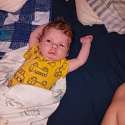 Ryker is registered to the contest to win money with this photo: arm, baby, bed, blanket, child, construction_print, curly_hair, cute, face, indoors, infant, lying_down, newborn, person, pillow, resting, sleepwear, soft_fabric, stretching, yellow_onesie