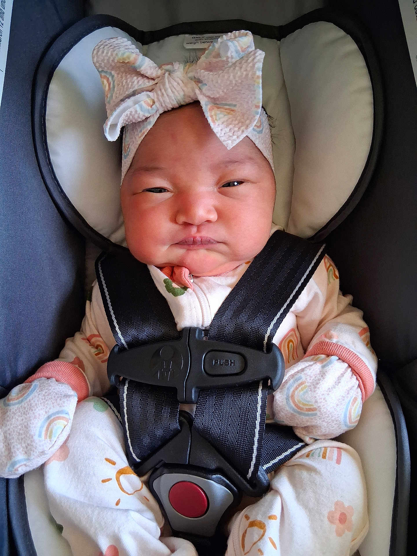 Rosèminá is registered to the contest to win money with this photo: baby, infant, car_seat, headband, bow, mittens, pajamas, rainbow_pattern, straps, safety_belt, face, person, cute, indoors, soft_lighting, child, newborn, apparel, expression, seated