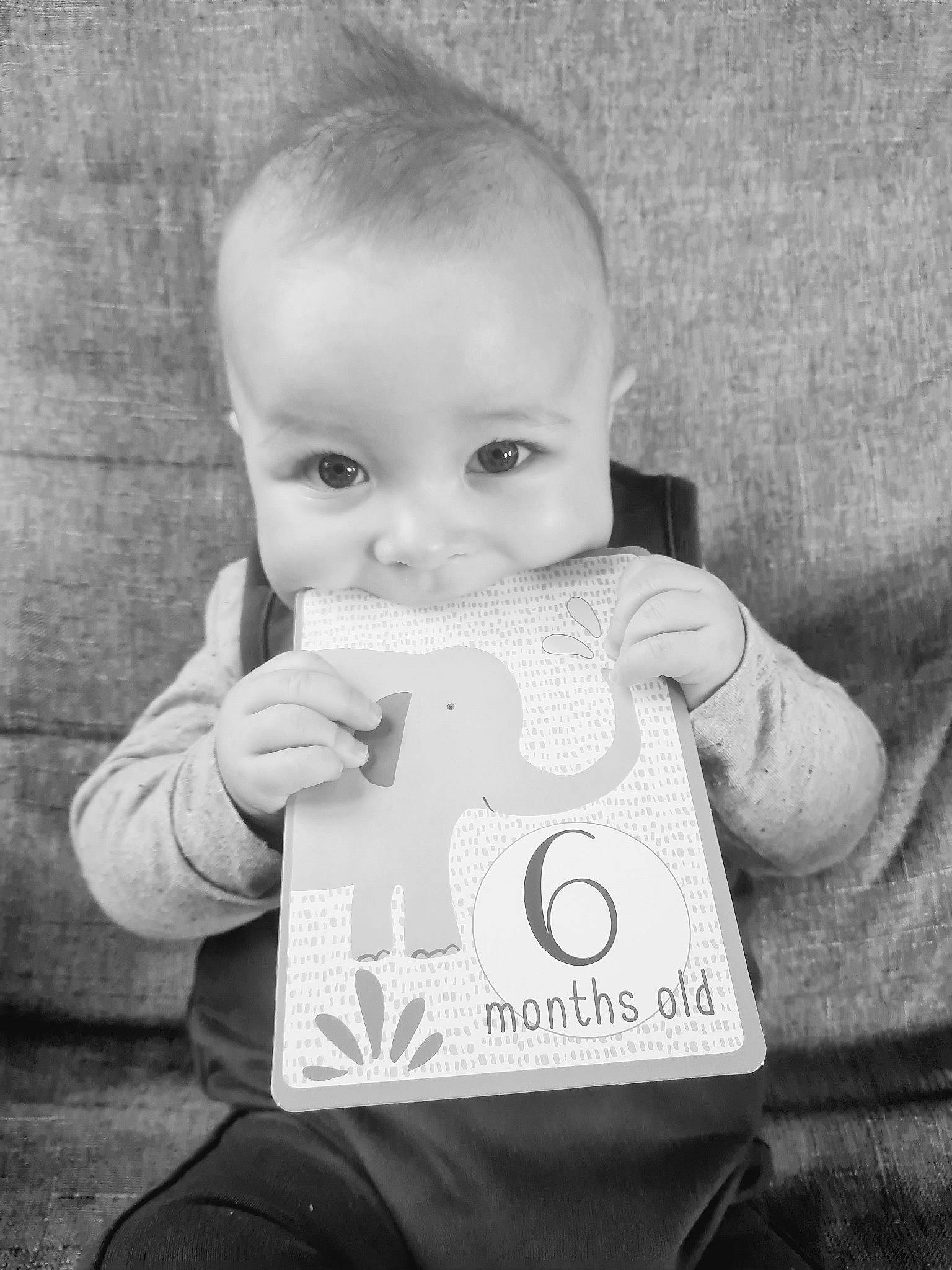 Gabriel a rejoint le concours — aidez-le/la à gagner de superbes lots ! arm, baby, baby_toddler_clothing, black_and_white, cheek, child, drinkware, eye, facial_expression, gesture, grey, hand, happy, human_body, iris, person, skin, sleeve, smile, style