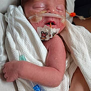 Connor is registered to the contest to win money with this photo: newborn, baby, infant, medical_tubes, hospital, towel, sleeping, face, arm, skin, person, healthcare, care, cute, teddy_bear_sticker, wrapped, peaceful, patient, medical_tape, resting