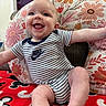 baby, smiling, infant, striped_clothing, nike, cushion, floral_pattern, indoor, red_blanket, happy, tongue_out, person, cute, seated, child, comfortable, soft_furniture, head, arms_outstretched, playful