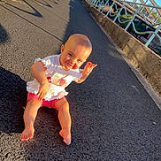 Lyanna a rejoint le concours — aidez-le/la à gagner de superbes lots ! toddler, child, barefoot, outdoor, sunny, pavement, bridge, blue_sky, smiling, playful, shorts, white_shirt, shadow, railing, concrete, nature, daylight, portrait, happy, casual