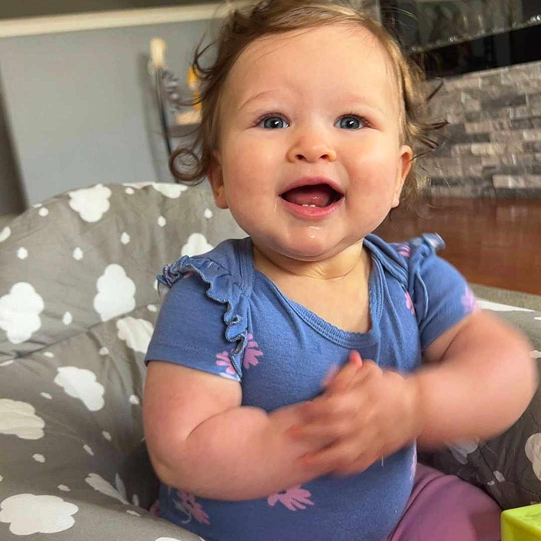 Hadley joined the competition — help win amazing prizes! baby, blue_eyes, blue_shirt, child, clapping, cloud_pattern, curly_hair, cushion, cute, fireplace, happy, indoor, living_room, person, pink_pants, playtime, sitting, smiling, stone_wall, toy_blocks