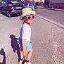 asphalt, blue_shorts, building, car, casual_clothing, child, daylight, footwear, hat, outdoor, person, shadow, sidewalk, smile, street, sunglasses, sunny, urban, white_shirt, woman