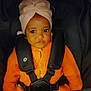 baby, child, infant, car_seat, orange_sweater, head_wrap, turban, seatbelt, cute, portrait, indoors, young_child, face, eyes, clothing, sitting, secure, adorable, warm_clothing, child_seat