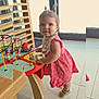 Maïwenne a rejoint le concours — aidez-le/la à gagner de superbes lots ! activity_table, bib, child, cute, daylight, floor, hair, happy, indoor, person, pigtails, pink_dress, play, shoes, smile, toddler, toy_beads, window, wooden_furniture, wooden_toy