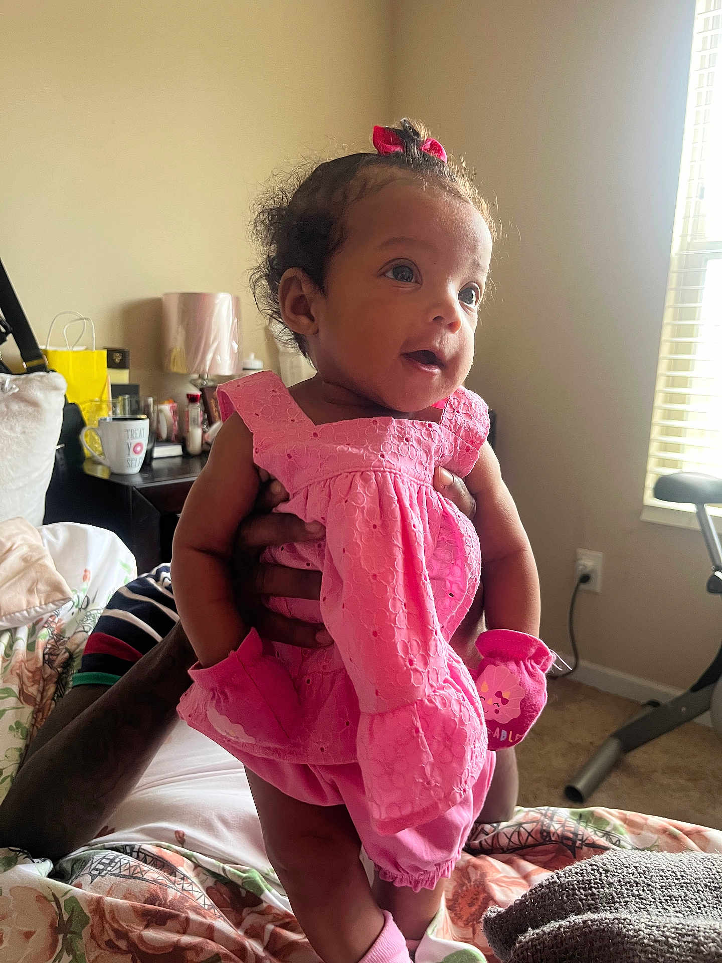 Sedora joined the competition — help win amazing prizes! baby, child, pink_clothing, dress, mittens, indoor, bedroom, window, natural_light, adult_hands, person, carpet, bed, pillow, lamp, table, cup, decor, portrait, smiling