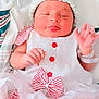 baby, infant, hat, knitted_hat, dress, white_dress, red_stripes, bow, button, blanket, hospital_bracelet, newborn, cute, face, tongue_out, sleepy, lying_down, soft_lighting, indoors, child