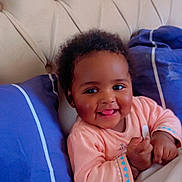 Lyanna a rejoint le concours — aidez-le/la à gagner de superbes lots ! baby, smiling, blanket, bed, blue_pillow, tufted_headboard, indoor, cozy, cute, happy, child, infant, sleepwear, person, portrait, relaxed, soft_lighting, resting, small_hands, playful