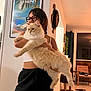 Roméo participe au concours pour gagner de l'argent avec cette photo : person, cat, glasses, indoor, home, wall_art, poster, cat_tree, floor_tile, pants, tank_top, furniture, balcony, curtain, light, smile, hair, large_cat, holding, relaxed