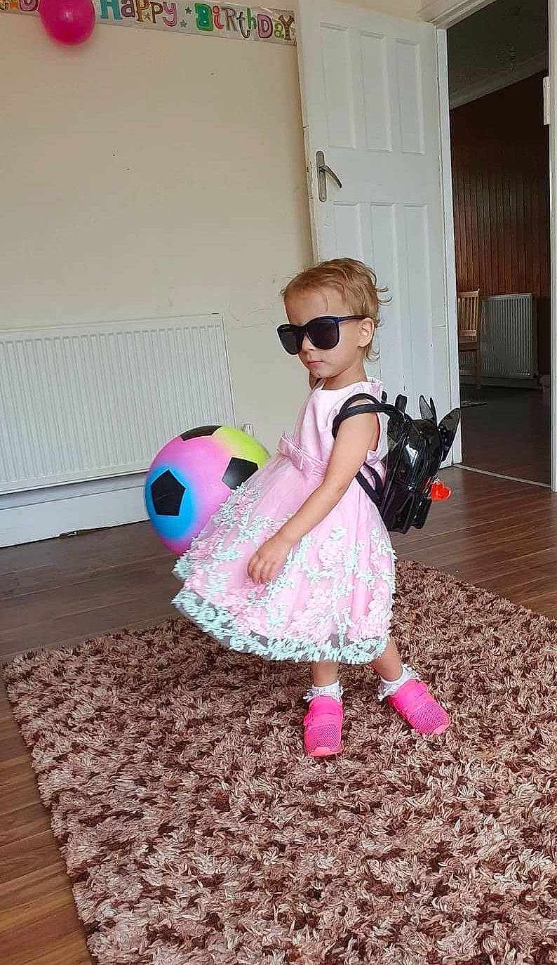 Adelina is registered to the contest to win money with this photo: baby, baby_toddler_clothing, day_dress, dress, fashion_accessory, floor, flooring, goggles, hardwood, laminate_flooring, magenta, party_supply, person, pink, play, stuffed_toy, sunglasses, toy, wood_flooring