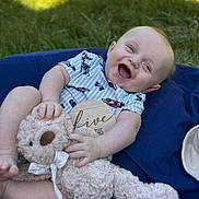 Owen is registered to the contest to win money with this photo: baby, teddy_bear, smiling, outdoor, grass, blue_cushion, infant, toy, happy, child, sitting, cute, plush, sunlight, joyful, clothing, person, portrait, head, playful