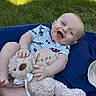 baby, teddy_bear, smiling, outdoor, grass, blue_cushion, infant, toy, happy, child, sitting, cute, plush, sunlight, joyful, clothing, person, portrait, head, playful