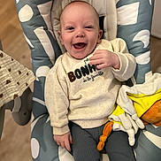 Elio a rejoint le concours — aidez-le/la à gagner de superbes lots ! baby, smiling, child, sweater, plush_toy, baby_chair, happy, indoor, portrait, clothing, person, infant, cute, seated, cozy, fabric, soft_toy, floor, expression, young_child