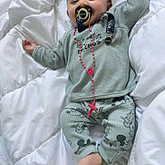 Abraham participe au concours pour gagner de l'argent avec cette photo : baby, infant, pacifier, pacifier_clip, rosary, cross_pendant, bedding, blanket, pajamas, mickey_mouse_pattern, smiling, face, toes, feet, hand, bed, cozy, green_outfit, newborn, playful