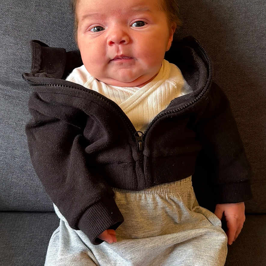 Joy participe au concours pour gagner de l'argent avec cette photo : apparel, baby, child, clothing, couch, cozy, cute, expression, face, hair, hoodie, indoors, infant, pants, person, portrait, sitting, skin, socks, young