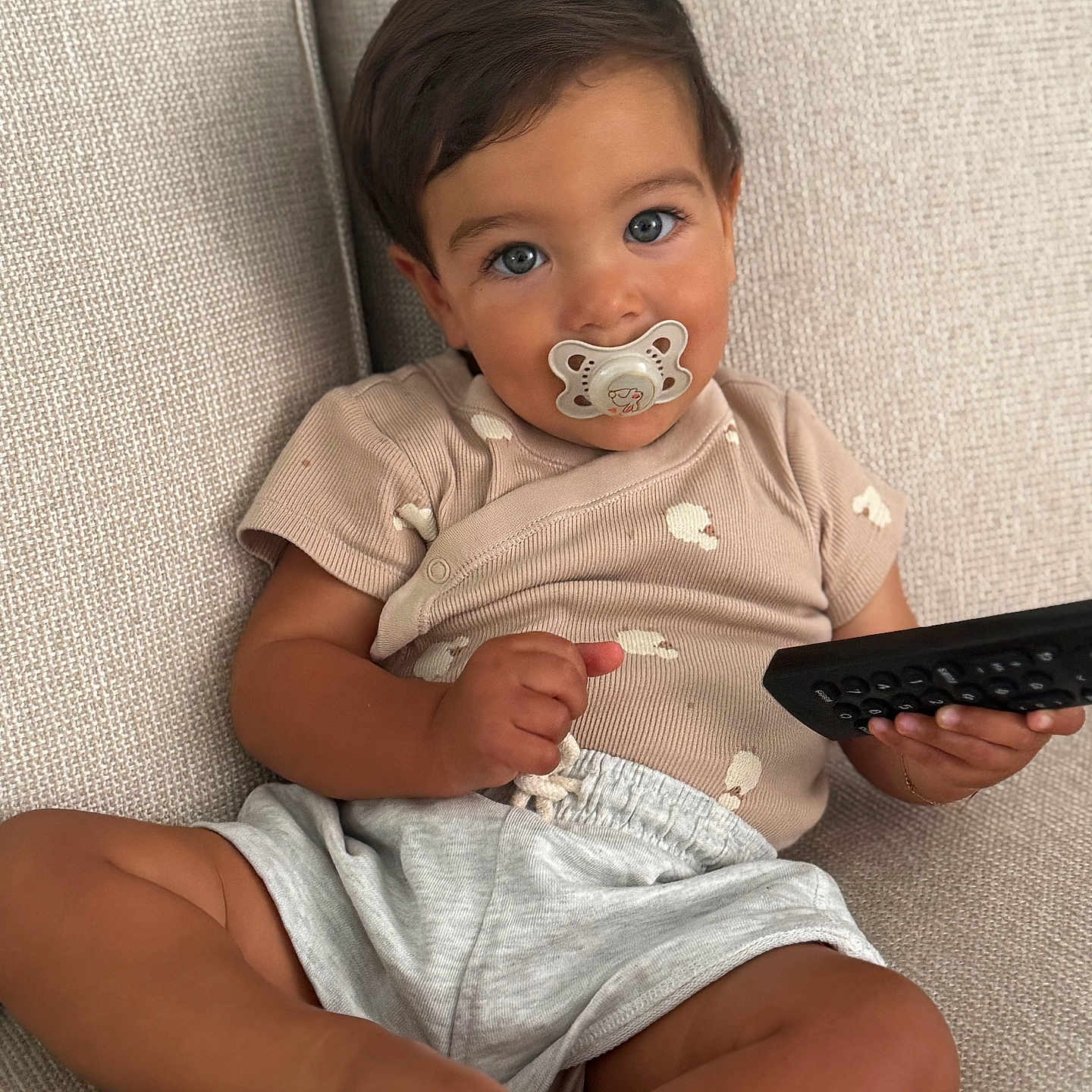 Nahyl participe au concours pour gagner de l'argent avec cette photo : baby, beige, blue_eyes, child, couch, cute, expression, face, feet, hands, indoors, infant, pacifier, relaxed, remote_control, shorts, sitting, skin, toddler, tshirt
