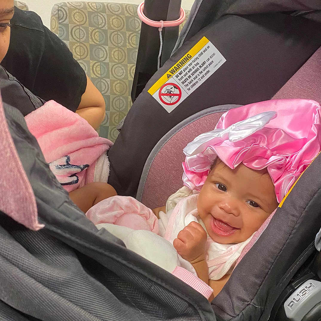 Saysri is registered to the contest to win money with this photo: adult, baby, blanket, car_seat, care, child, closeup, clothing, cute, family, furniture, happy, headwear, indoor, infant, person, pink_bonnet, portrait, seat, smiling