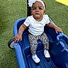 baby, child, infant, portrait, sitting, ride_on_cart, blue_cart, outdoor, artificial_grass, headband, flower, white_clothing, leopard_print, pants, shoes, serious_expression, looking_at_camera, furniture, play_equipment, photography