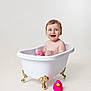 toddler, child, bathtub, bath, bubbles, pink_sponge, rubber_duck, toy, white_tub, clawfoot_tub, smiling, happy, baby, bath_time, clean_background, studio_shot, indoor, cute, playful, water