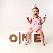 Millie joined the competition — help win amazing prizes! baby, child, one_year_old, birthday, crown, pink_romper, white_blocks, wooden_letters, letter_o, letter_n, letter_e, studio_photo, smiling, happy, celebration, sitting, barefoot, cute, portrait, isolated_background