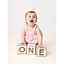 Millie is registered to the contest to win money with this photo: baby, child, birthday, crown, pink_outfit, blocks, one, happy, smiling, celebration, studio, white_background, cute, infant, portrait, hands, kneeling, young, cheerful, first_birthday
